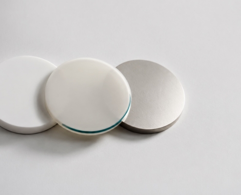 Three material sample discs in porcelain, translucent ceramic, and brushed metal, representing dental crown material options.