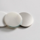 Three material sample discs in porcelain, translucent ceramic, and brushed metal, representing dental crown material options.