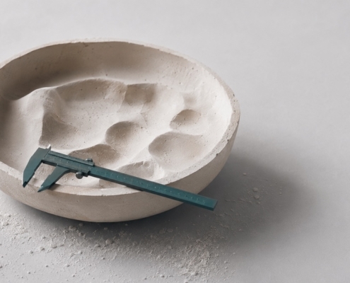 A plaster casting mould with a teal calliper resting in it, representing the denture fitting and adjustment process.